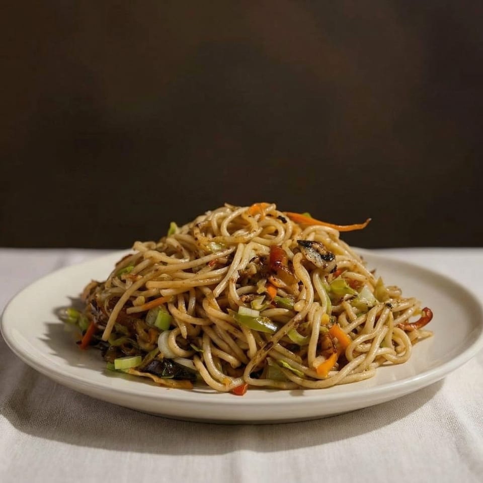 A plate of stir-fried noodles with vegetables like carrots, cabbage, and green onions.