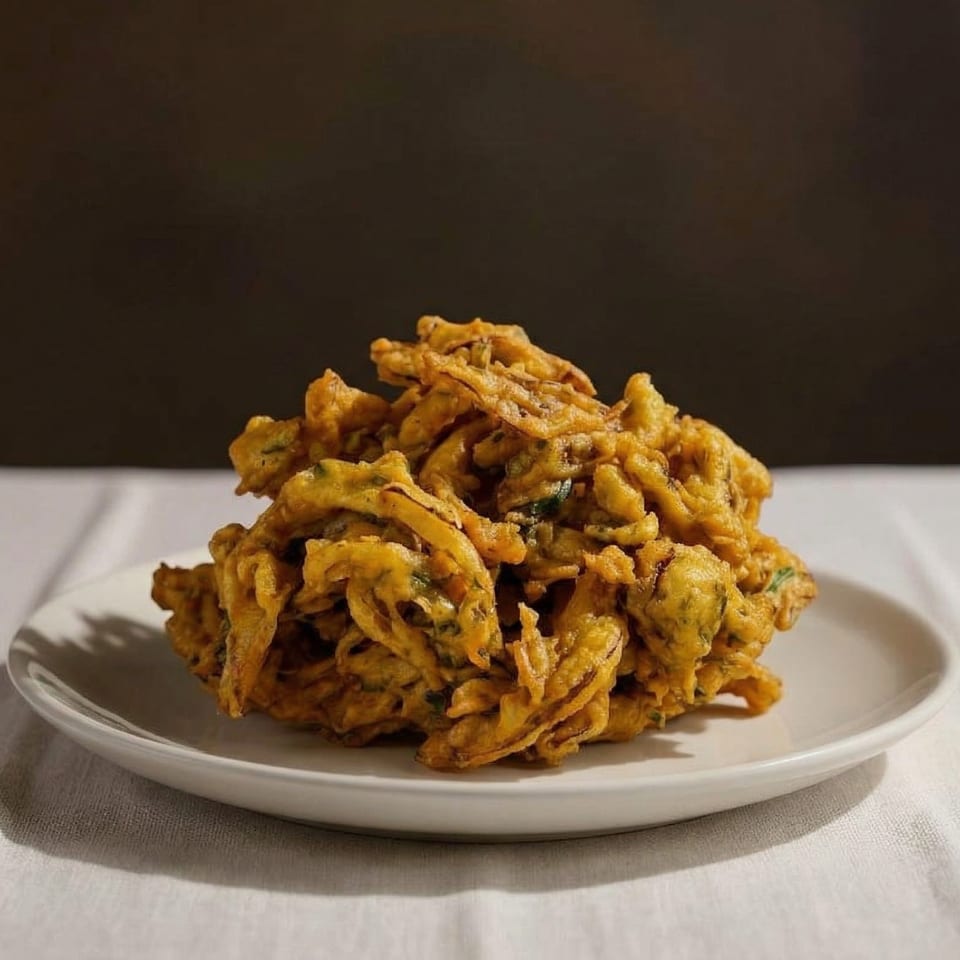 A large pile of golden-brown, crispy fried pakora sits on a white plate.